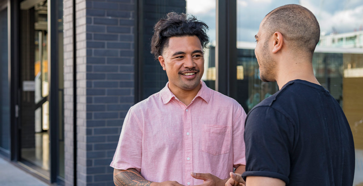 1. Two men engaged in conversation outside a building, with one gesturing while the other listens attentively.