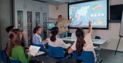 A teacher standing at a whiteboard while explaining a detailed public health map.