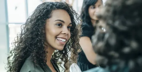 Professional woman smiling at a colleague while discussing women's leadership and career empowerment strategies.